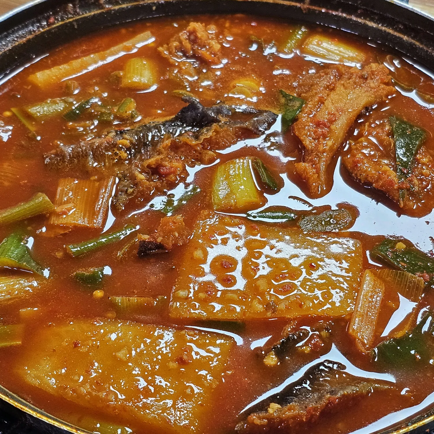 끓고 있는 북어물찜 — 붉은 국물 속 북어 조각, 넓적하게 썬 무, 대파